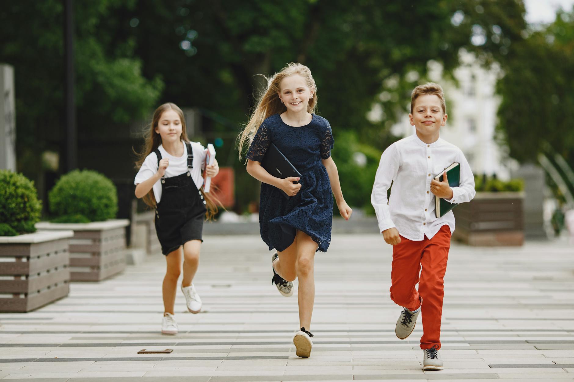 Three kids running joyfully on a sunny sidewalk, symbolizing fun and friendship.